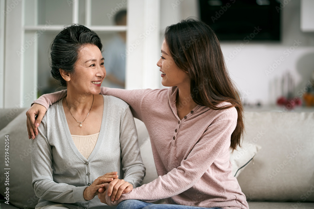 asian adult daughter and senior mother sitting on couch at home chatting talking conversing asian adult daughter and senior mother sitting on couch at home chatting talking conversing