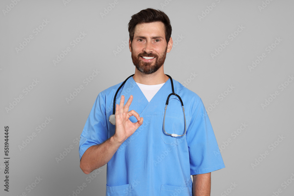 Doctor with stethoscope showing okay gesture on light grey background Doctor with stethoscope showing okay gesture on light grey background