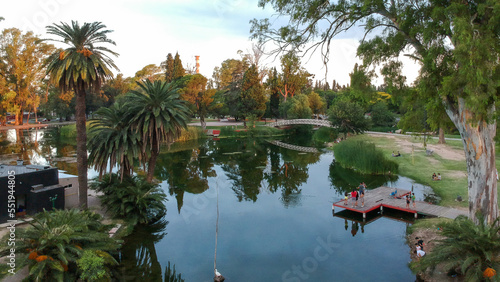 Lago con un puente rodeado de palmeras y arboles con gente y reflejo del agua