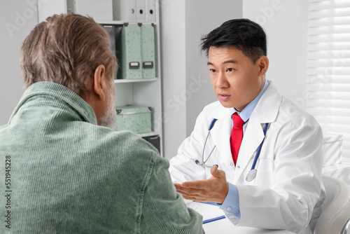 Doctor consulting senior patient at white table in clinic