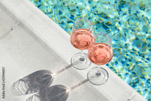 Fototapeta Naklejka Na Ścianę i Meble -  Glasses of tasty rose wine on swimming pool edge, space for text