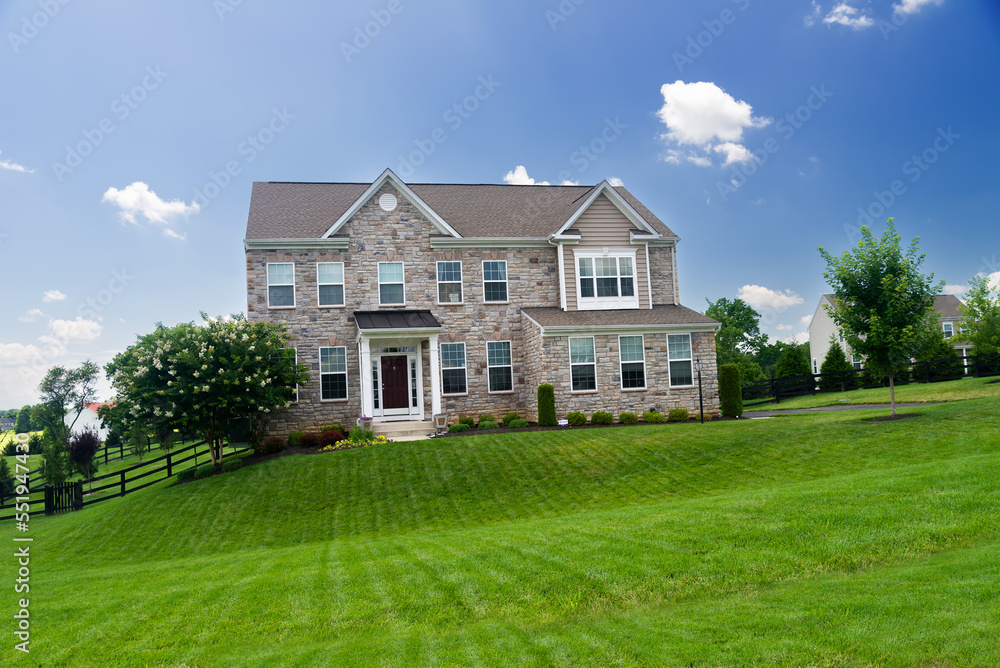 large, luxurious, brick house with landscaping and a huge green lawn. Landscape on a summer sunny day under a blue cloudy sky. large, luxurious, brick house with landscaping and a huge green lawn. Landscape on a summer sunny day under a blue cloudy sky.