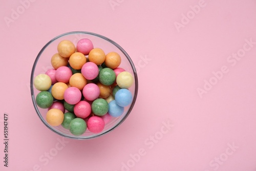 Bowl with many bright gumballs on pink background  top view. Space for text