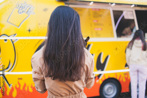 Girl choosing and ordering street food in colourful food truck van on a festival in a city park, summer sunny day, food stall kiosk offers fast food, coffee and drinks for sale