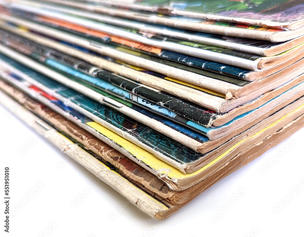 Closeup of a stack of vintage comic books with faded and worn pages isolated on white background