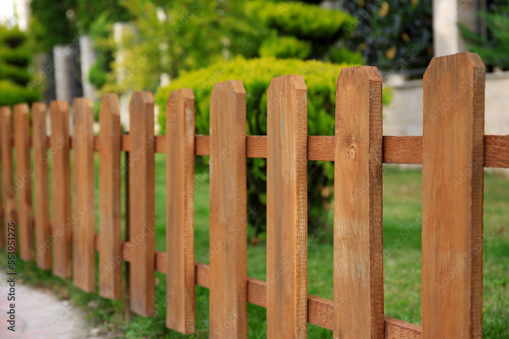 Closeup view of small wooden fence near green bushes in garden