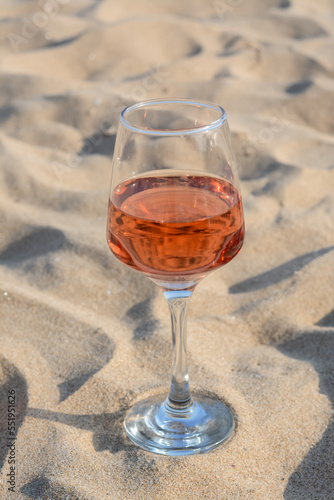 Glass of tasty rose wine on sand