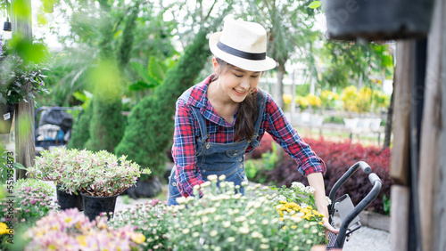Gardening blossom and Asian woman people concept - happy smiling Adult female in apron with flower care fertilizer at summer garden. Agriculture florist smiling activity happy hobby 