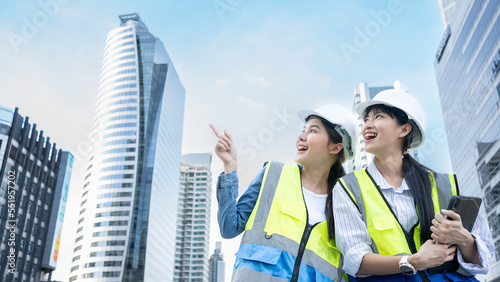 Portrait of two professional Asian engineer or technician workers stand look at camera with smiling and arm-crossed on City  of construction site and day light. Woman in Engineering project manager.