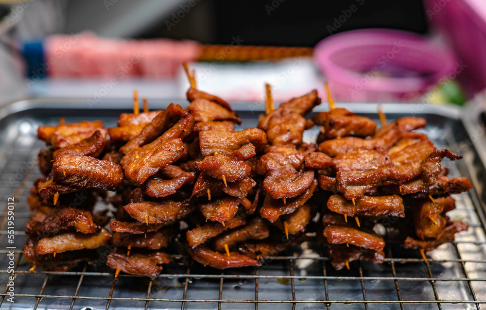 Fried pork skewers on bamboo sticks for sale along the sidewalk in Bangkok, Thailand