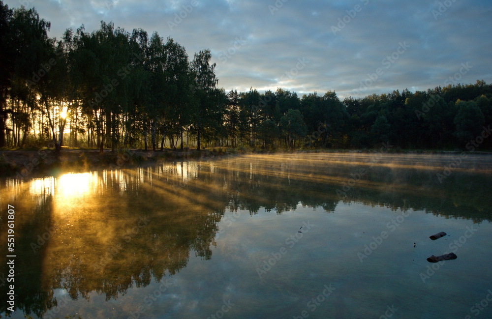 Naklejka premium Morning sun rays on the water of a small lake. Moscow region. Russia