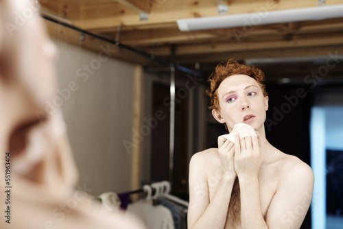 Young man standing in front of mirror removing his make up using cleansing wipes