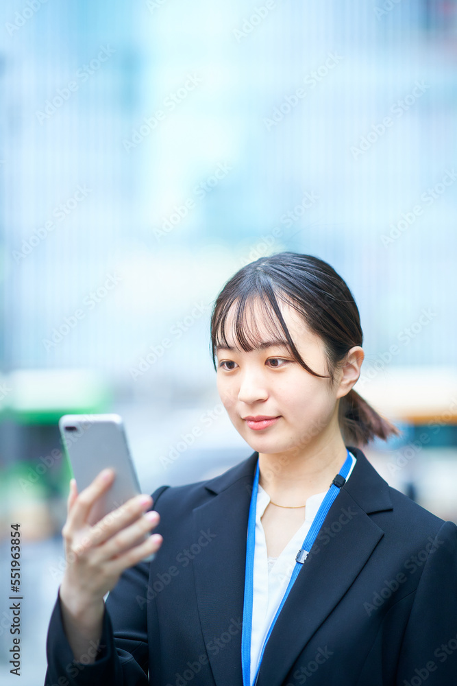 スマートフォンの画面を見るスーツ姿の若い女性 スマートフォンの画面を見るスーツ姿の若い女性
