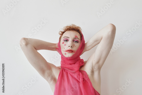 Fashion portrait of young man wearing pink outfit with clownlike make-up posing on camera