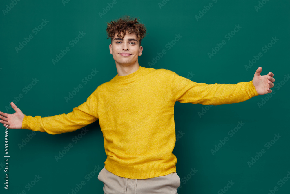 a joyful, smiling man stands on a green background in a yellow sweater and spreads his arms wide, smiling pleasantly