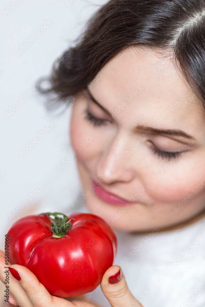 A young woman with a juicy tomato in her hand. Healthy food and vegetarianism. Close-up. Vertical. Selective focus. A young woman with a juicy tomato in her hand. Healthy food and vegetarianism. Close-up. Vertical. Selective focus.
