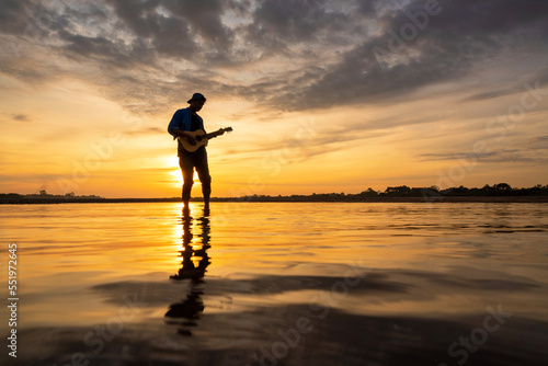 Silhouette of musician with guitar in the river and Beautiful cloudy sky at sunrise in the early morning for background. © tong2530