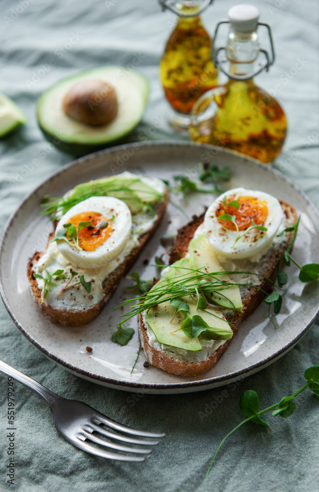 Bread toast, boiled eggs, avocado slice, microgreens on a plate