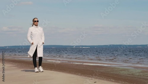 a beautiful woman with red hair in a white coat walks on a sandy beach on a cold sunny day