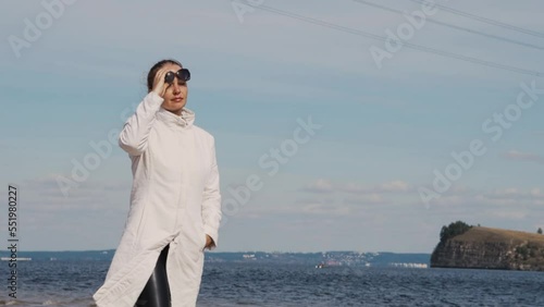 a beautiful woman with red hair in a white coat walks on a sandy beach on a cold sunny day