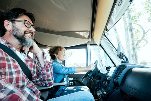 Woman driver driving a camper van with happy man on passenger seat. Alternative couple enjoying travel and van motorhome holiday vacation and lifestyle. Empowerment female people drive a truck