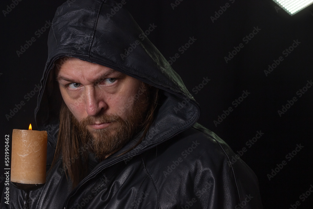 Portrait of a man in a cloak with a hood against a dark background with a candle on candlestick Portrait of a man in a cloak with a hood against a dark background with a candle on candlestick