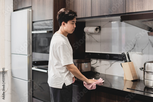 Asian man is cleaning the countertop with towel.