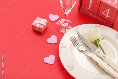 Cube calendar with date 14 FEBRUARY, table setting and hearts on red background, closeup