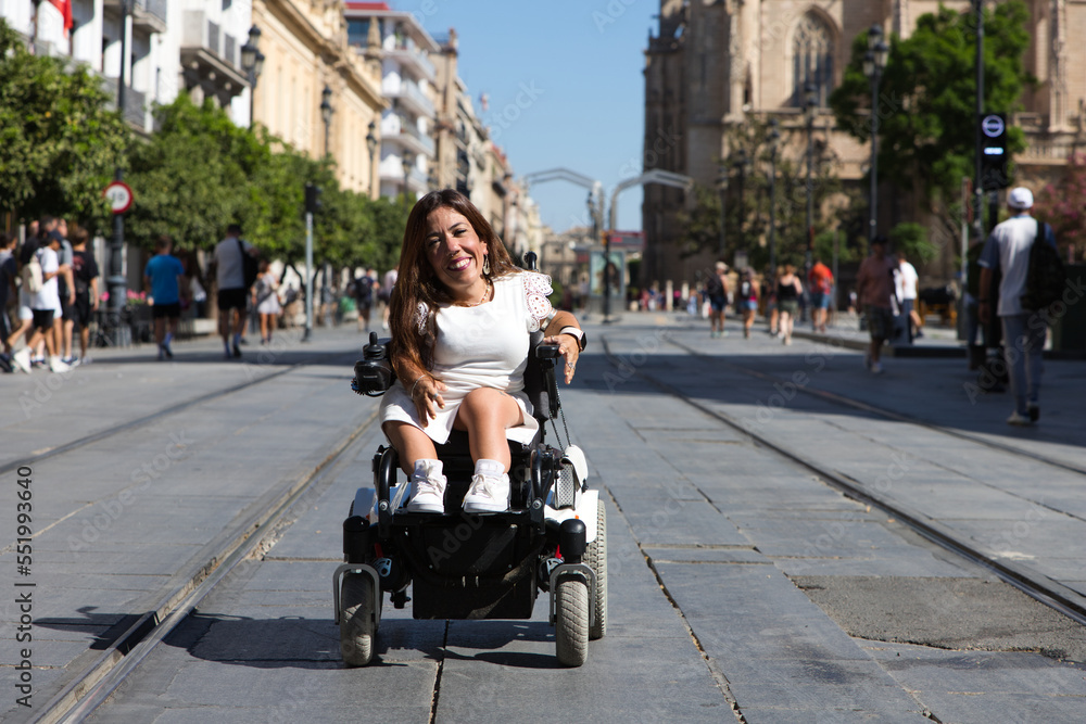 Obraz premium beautiful young disabled woman in wheelchair and reduced mobility enjoys her trip around the city where she is on vacation.