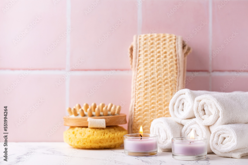 Spa setting with  burning canles, towels, wisk, massager against pink tiled wall.   Beauty blogging, salon  care concept. Selective focus. Place for text.