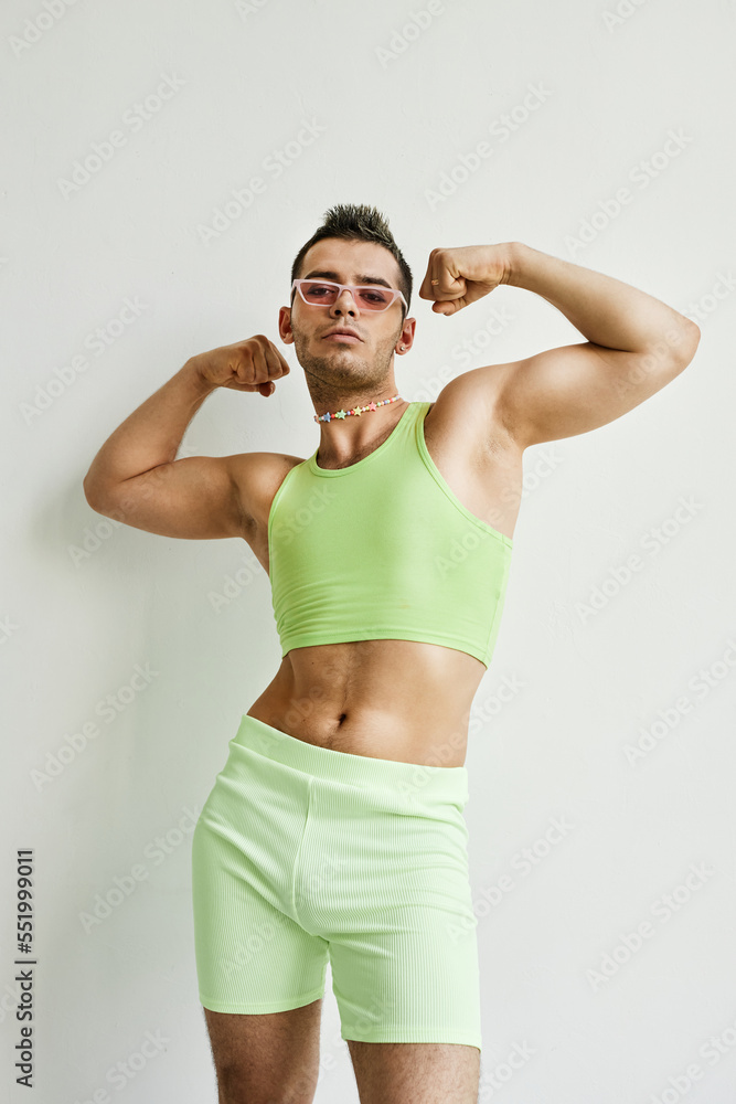 Portrait of muscular non binary man posing against white in studio wearing neon green crop top Portrait of muscular non binary man posing against white in studio wearing neon green crop top