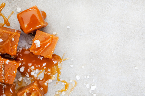 Salted caramel, a taste sensation. Coarse salt and caramel blocks covered in a sticky creamy salted caramel sauce on grey photo