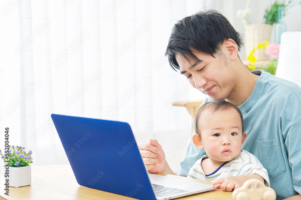 家で赤ちゃんとパソコンを見る父親 家で赤ちゃんとパソコンを見る父親