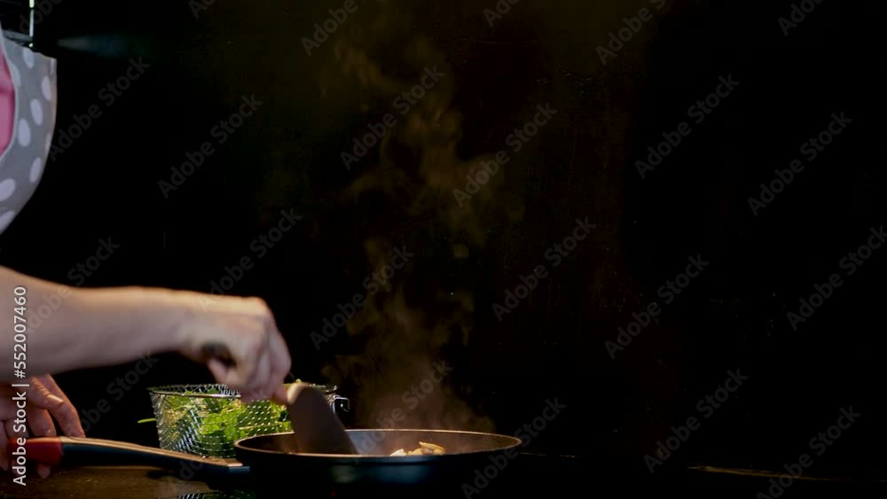 A woman in an apron cooks at home in the kitchen. Frying champignons in a frying pan, close-up A woman in an apron cooks at home in the kitchen. Frying champignons in a frying pan, close-up