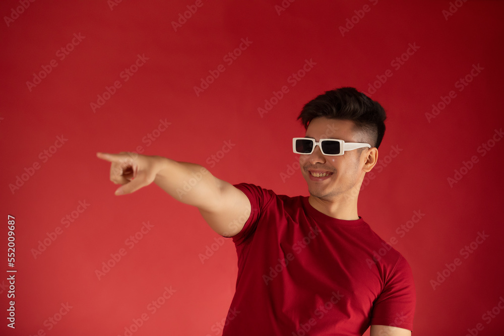Young man in sunglasses pointing away against red background Young man in sunglasses pointing away against red background