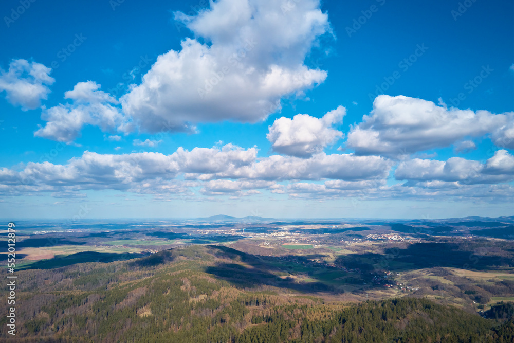 Clouds in blue sky with shadows on ground. A birds eye view of beautiful mountains covered with evergreen forest on sunny autumn day. Natural landscape with mountain ranges and valleys