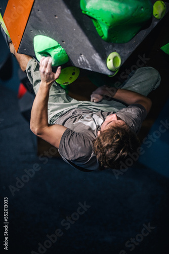 A young, athletic guy with a beautiful inflated body climbs a bouldering in a climbing hall. Emotions on the face.