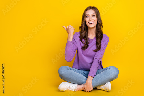Full length portrait of cheerful nice person sit floor look direct finger empty space isolated on yellow color background photo
