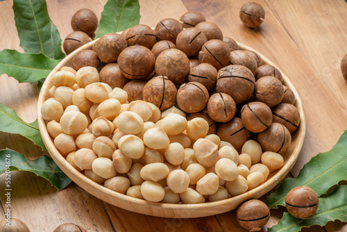 Macadamia nuts with leaf and Macadamia with hard shell on wooden plate on wooden background.