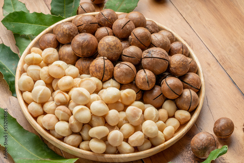 Macadamia nuts with leaf and Macadamia with hard shell on wooden plate on wooden background.