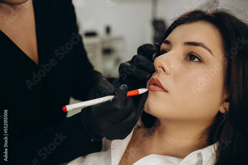 Beauty stylist making lips shape before permanent makeup procedure at the cosmetic salon