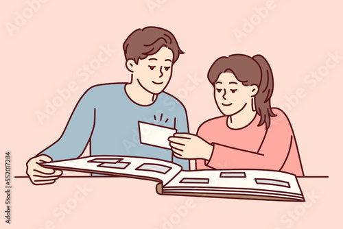 Happy couple man and woman looking at family photo album with pictures from wedding or vacation. Casual guy and girl sits at table remember past together enjoy watching photo cards. Flat vector image