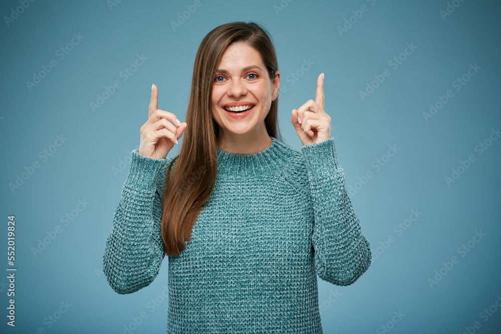 Smiling woman in casual warm clothes pointing fingers up. Advertising female studio portrait on blue. Smiling woman in casual warm clothes pointing fingers up. Advertising female studio portrait on blue.