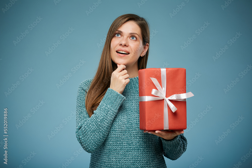 Happy woman in green sweater holding red gift thinking and looking up. Advertising female studio portrait. Happy woman in green sweater holding red gift thinking and looking up. Advertising female studio portrait.