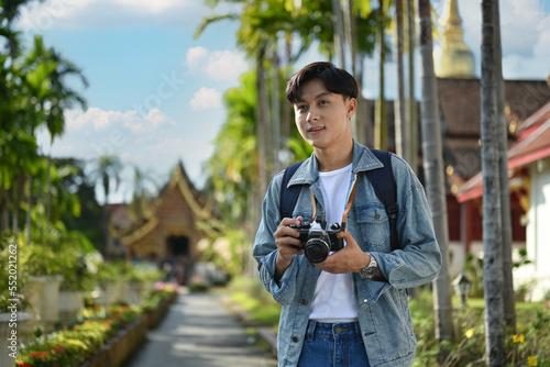 Young photographer tourist with camera standing outdoor with beautiful sky and buddhist temples on background