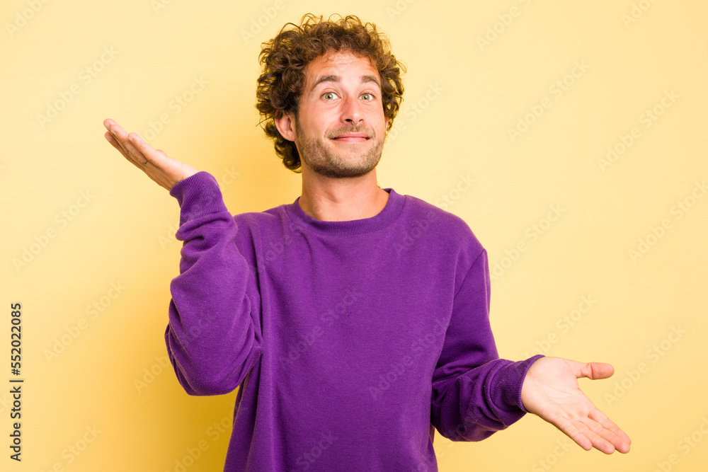 Young smart caucasian man on yellow background confused and doubtful shrugging shoulders to hold a copy space. Young smart caucasian man on yellow background confused and doubtful shrugging shoulders to hold a copy space.