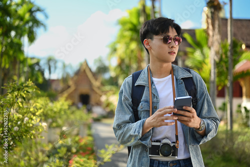 Man traveler using smart phone while standing outdoor with beautiful sky and buddhist temples on background