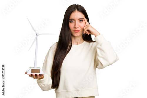 Young caucasian woman holding a small wind energy mill isolated pointing temple with finger, thinking, focused on a task.