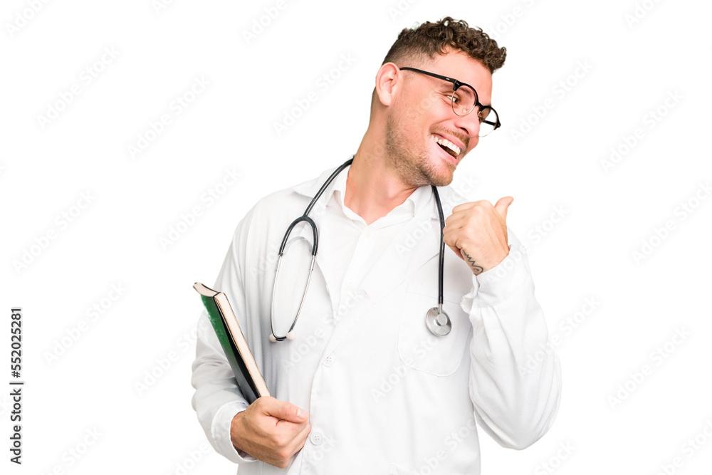 Young doctor caucasian man holding a book isolated points with thumb finger away, laughing and carefree. Young doctor caucasian man holding a book isolated points with thumb finger away, laughing and carefree.