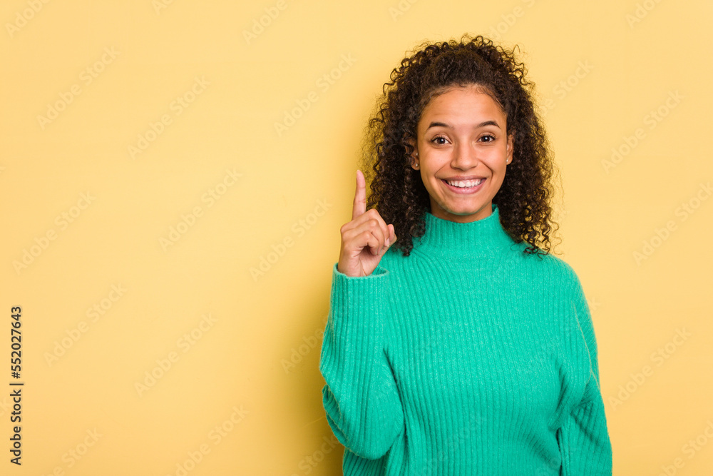 Young Brazilian curly hair cute woman isolated on yellow background showing number one with finger. Young Brazilian curly hair cute woman isolated on yellow background showing number one with finger.